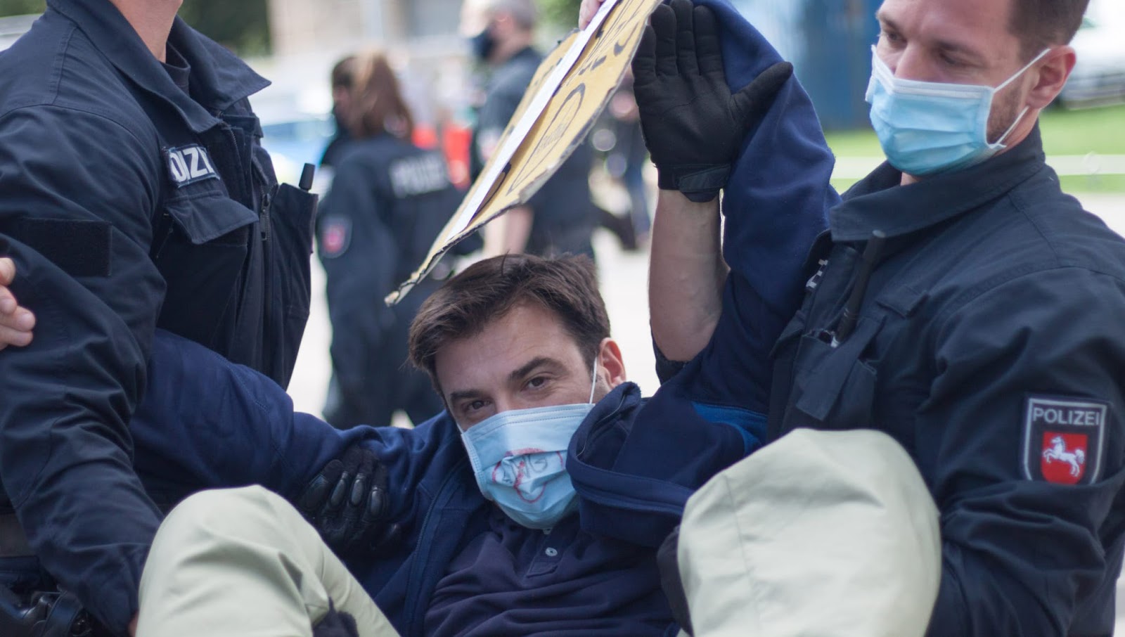 Wearing a face mask and carrying a placard, Esteban Servat is carried away by two poliemen.